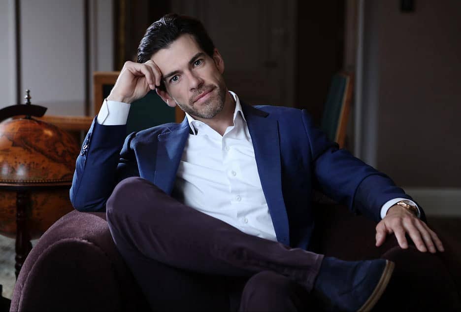 Stylish corporate headshots of a male professional posing in a blue blazer and dark trousers within a sophisticated study with a globe background.